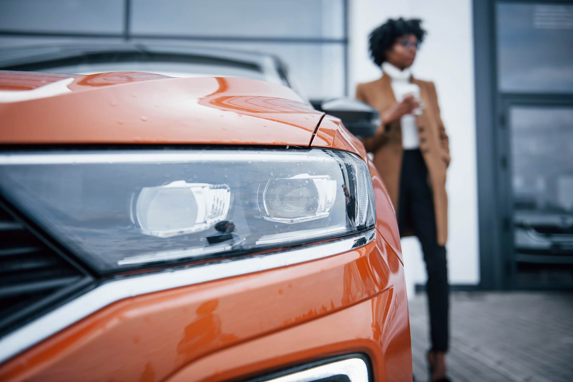 Close-up orange premium rental car front headlights LED modern SUV wet hood city background
